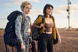 Julia Garner and Jessica Henwick squint in the outback, wearing huge backpacks, in the film The Royal Hotel.