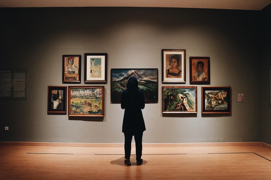 A person looks at artworks hanging on a wall in a gallery.