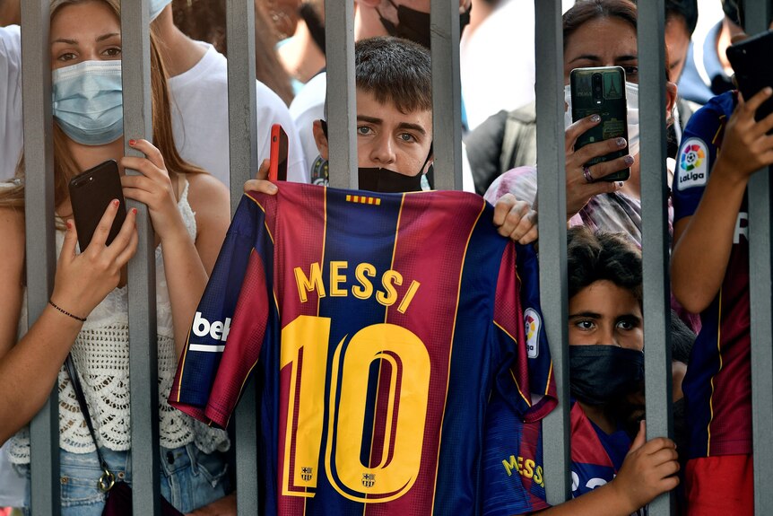 A boy holds up Messi's No. 10 jersey outside the gates of Camp Nou Stadium during the press conference