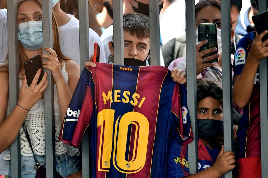 A boy holds up Messi's No. 10 jersey outside the gates of Camp Nou Stadium during the press conference