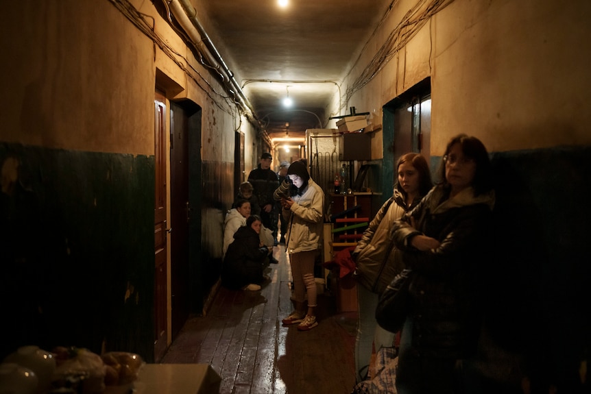 A group of stand around in a dark apartment building hallway