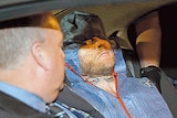 A man wearing forensic coveralls in a car