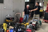 Two men looking at a pile of flooded tools.