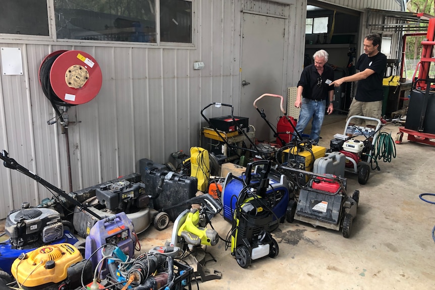 Two men looking at a pile of flooded tools.