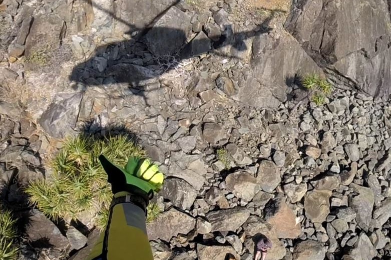 On of the men sits on the rocky terrain as a member of the rescue crew gives the thumbs up from the helicopter.