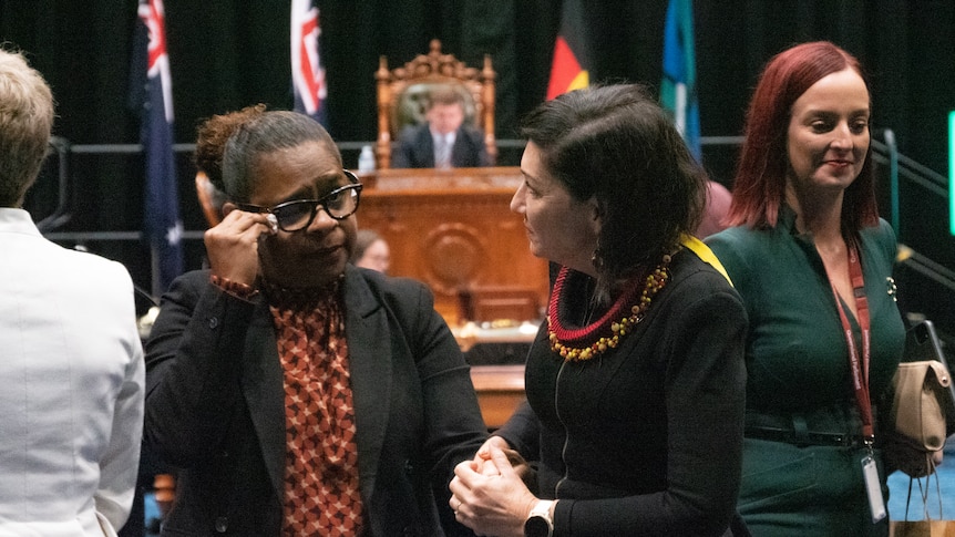 two women, one wiping away tears, standing in Queensland parliament