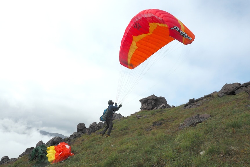 A mam launches a parachute on a steep, grassy mountain side.