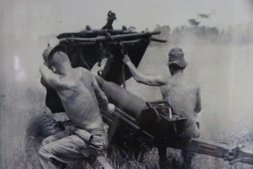 Black and white photo of two young men shirtless operating weaponry. 