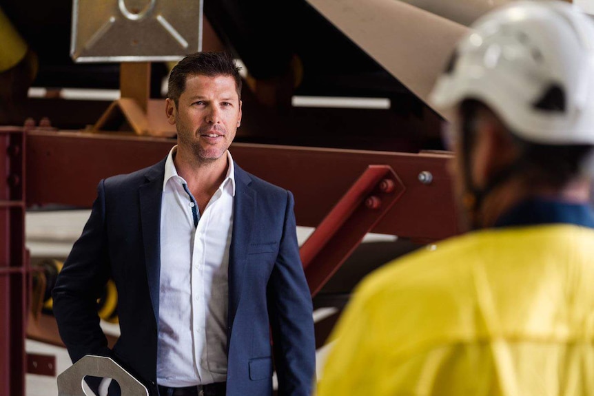 Mid shot of a man in a suit talking to a man in high-vis wear.