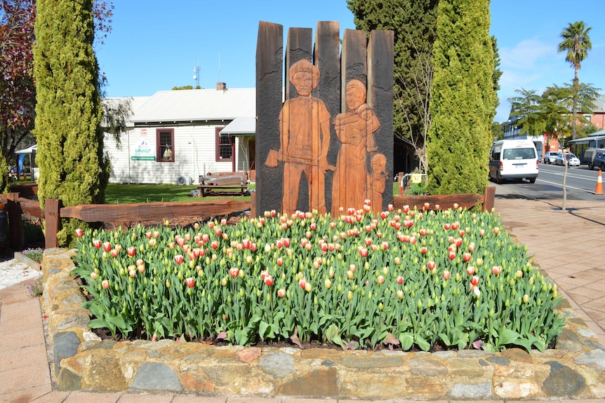 A sculpture depicting a lumberjack and his family. It is set amongst a bed of flowers in a small town.