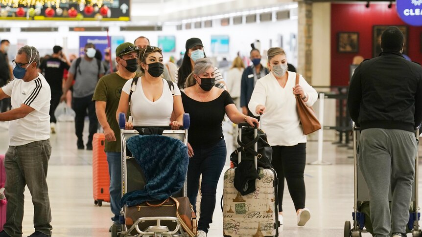 Travellers wearing face masks walk through an airport decorated with Christmas ornaments