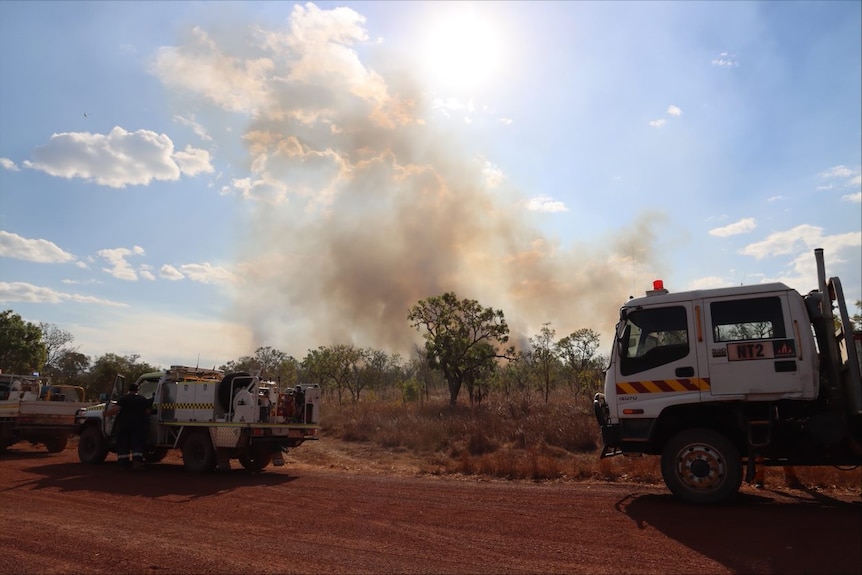 A photo of a fire truck with smoke emerging from bush land in the background.