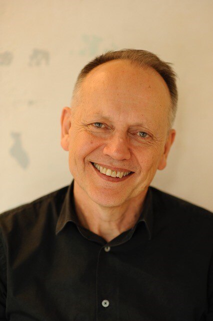 A man, Greg Dore, wearing a black button up shirt and jacket.