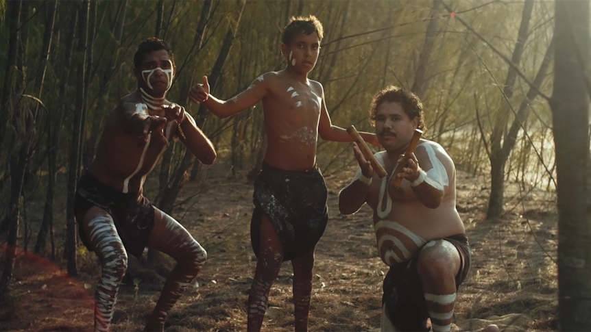 Three boys dancing together in a beach-side thicket.