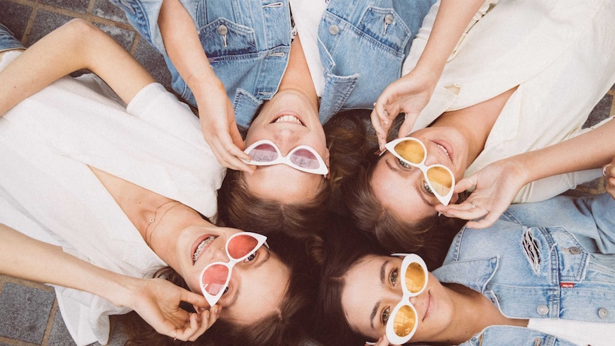 four band members lying on ground with sunnies