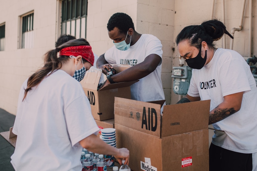 A group of volunteers wearing white t-shirts and face masks unpacking cardboard boxes