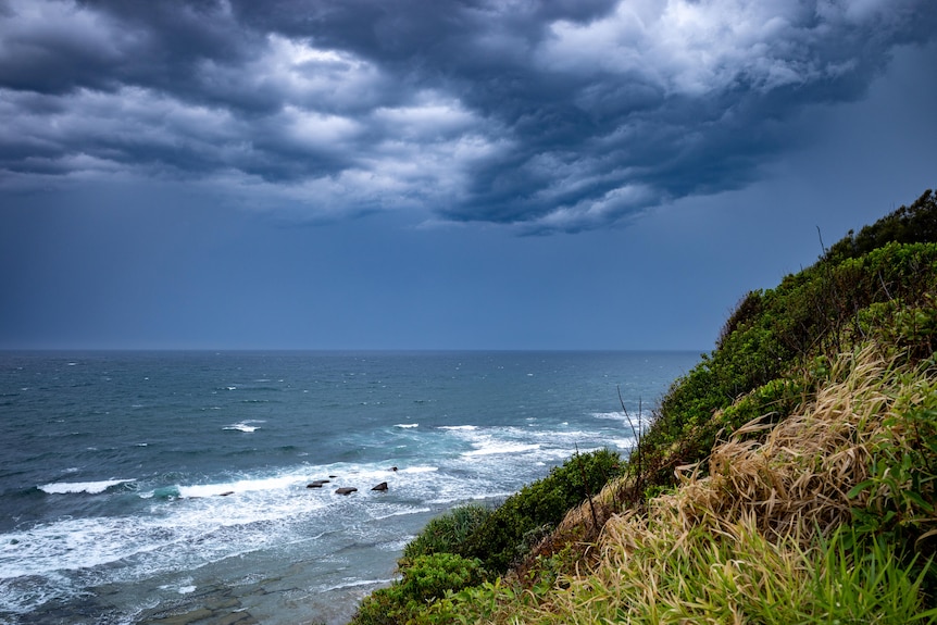 dark storm clouds rolling in over a beachside cliff. the waves look choppy and the sky is dark