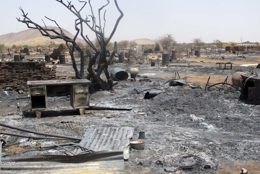 A desert town scorched by fire with the shells of corrugated iron and a desk in the foreground.