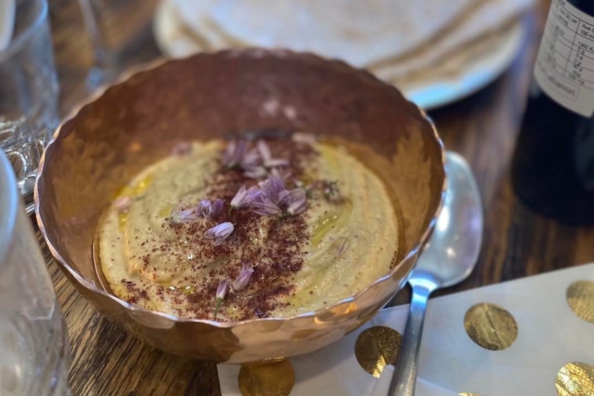A bowl of hummus tip garnished with purple flower petals and olive oil.