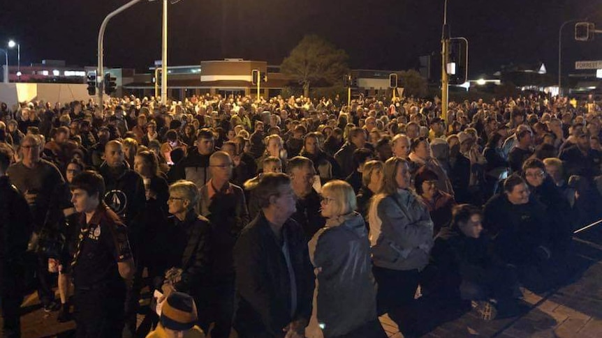 Crowds of people stand under a streetlight in a roadway intersection
