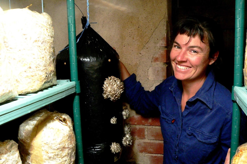 A close shot of Ella McHenry standing in a small room next to a black bag full of mushrooms.