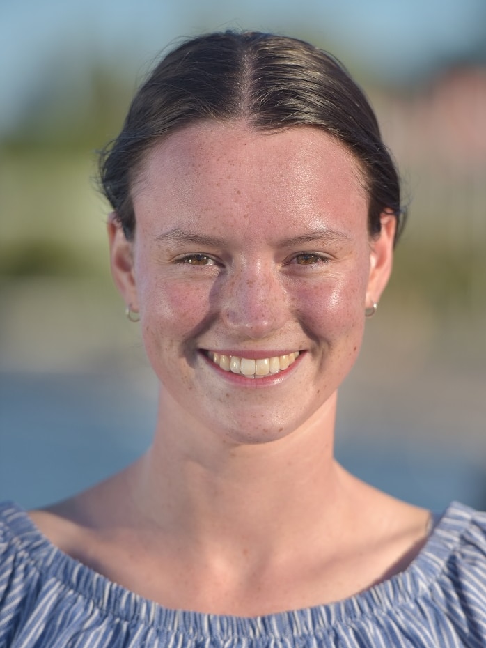 A head shot of a smiling young woman in a blue shirt with her hair pulled back.