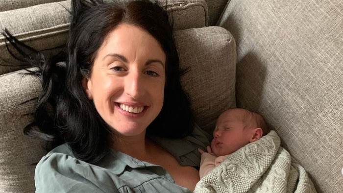 Woman laying down on the couch while holding her baby in her arms 