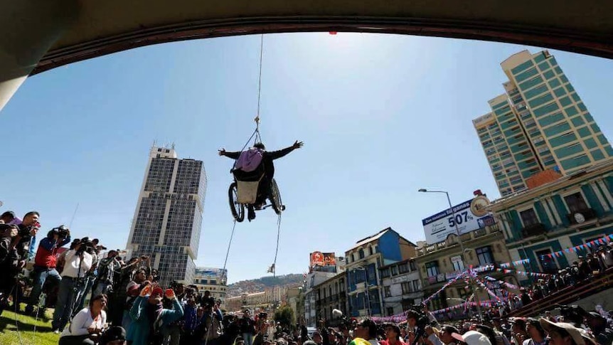 A disabled protester in a wheelchair is suspended from a bridge in Bolivia.