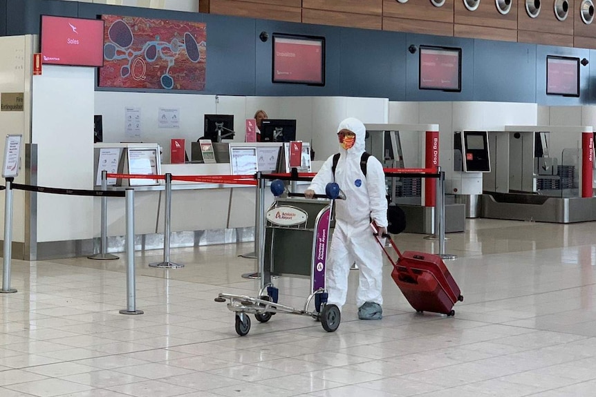 A person wearing a white protective suit walking in Adelaide Airport
