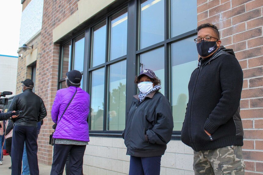 People standing in a line outside a building rugged up in coats and face masks