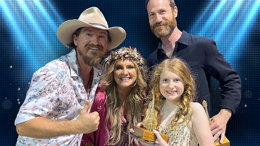Tiggy holds a golden guitar trophy on stage with her family.