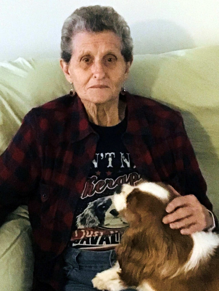 Helen sits on a couch with her dog on her lap.