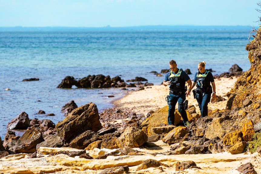 Two uniformed police officers walking along a rocky stretch of beach.
