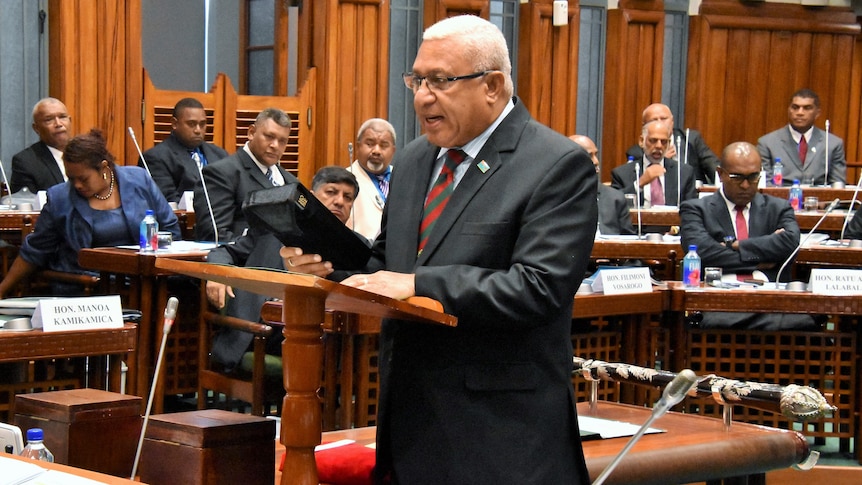Frank Bainimarama holds bible while in parliament.