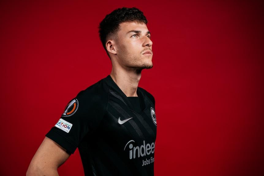 A male soccer player wearing black poses in front of a red background