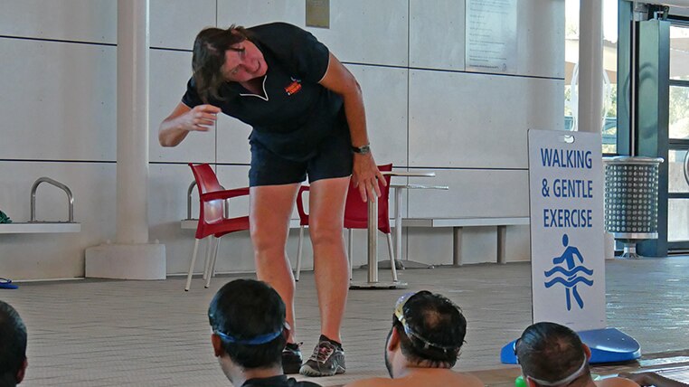 A woman stands on the side of a swimming pool, teaching adults to swim