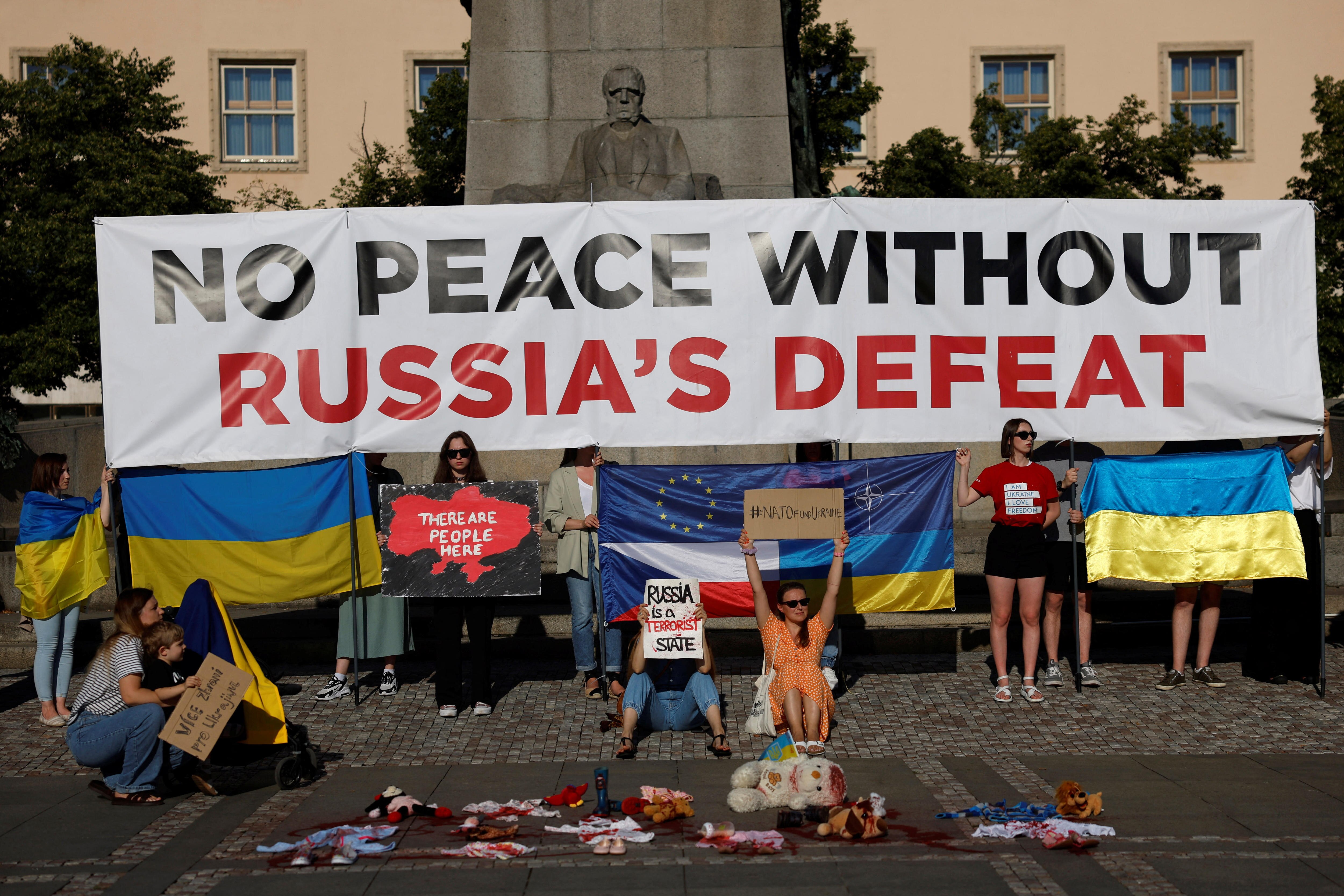 Protesters sitting on a roadside holding up a sign reading 'No Peace without Russia's defeat'