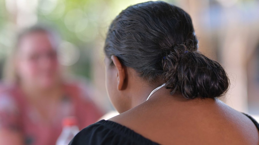 A woman's back is to the camera. Her hair is in a ponytail and she is wearing a black shirt.