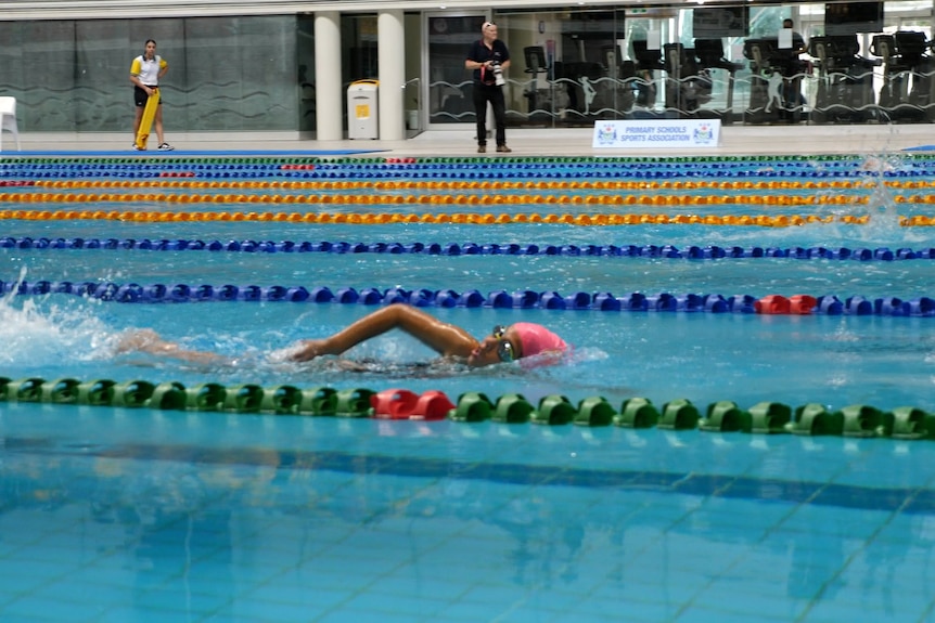 A young girl takes a breath while swimming freestyle in an Olympic pool.