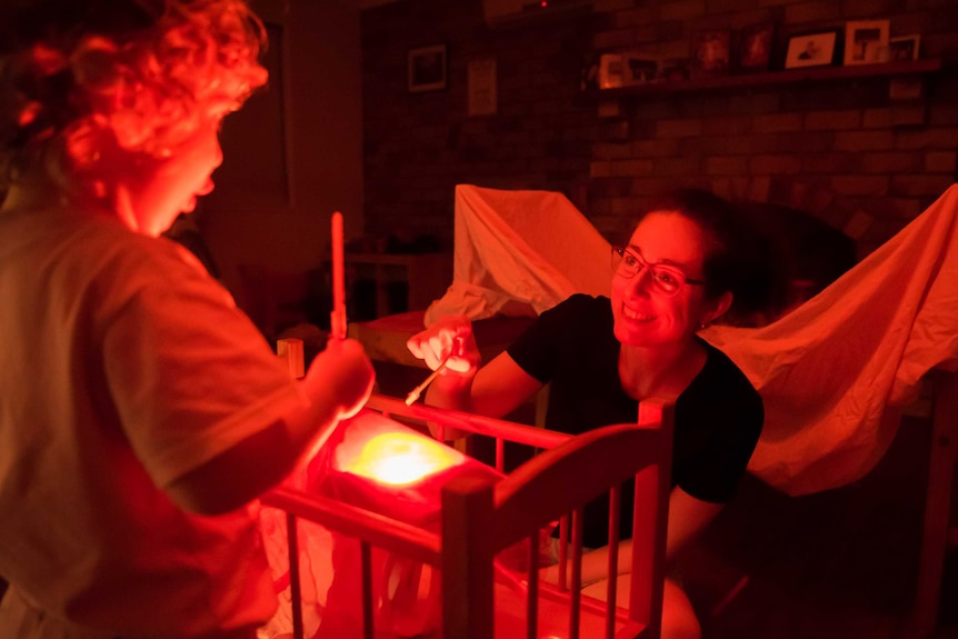 A mother and daughter roast marshmallows around a pretend campfire in their living room.