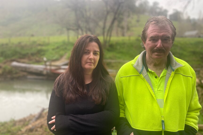 A dark-haired woman stands on a soggy country property with an older man, who is wearing high-vis.