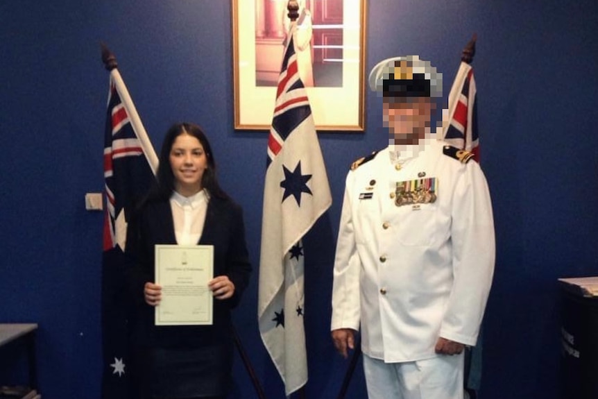 Teri Bailey with a man in a white uniform stand in front of Australian flags.
