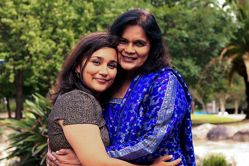 Two women embracing for a photo standing in front of green trees