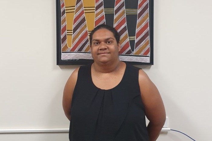 portrait of woman looking at camera standing in front of a painting hanging on a wall