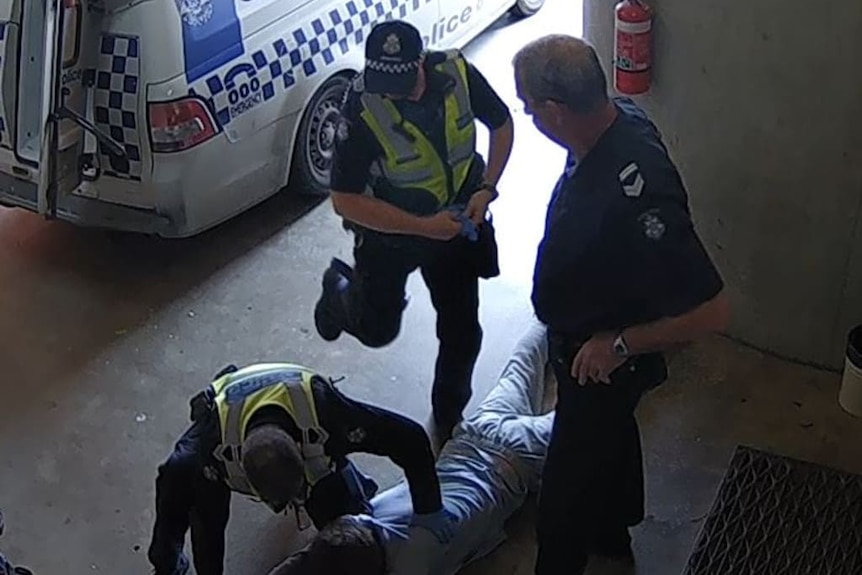 A still taken from CCTV footage showing a police officer swinging his leg back in preparation to kick a man lying on the ground.