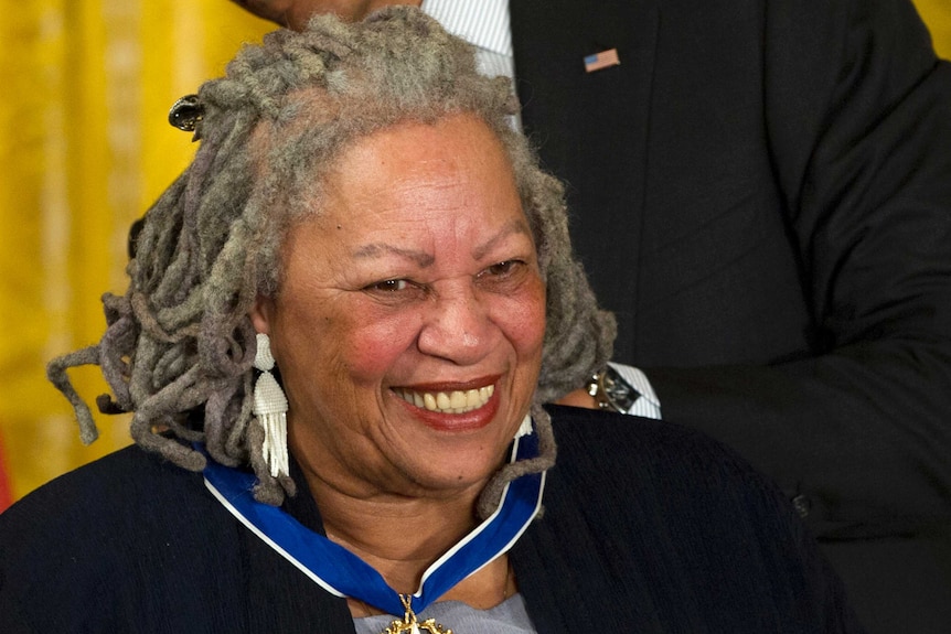 A black woman with grey dreadlocks smiles as a medal is places around her neck.