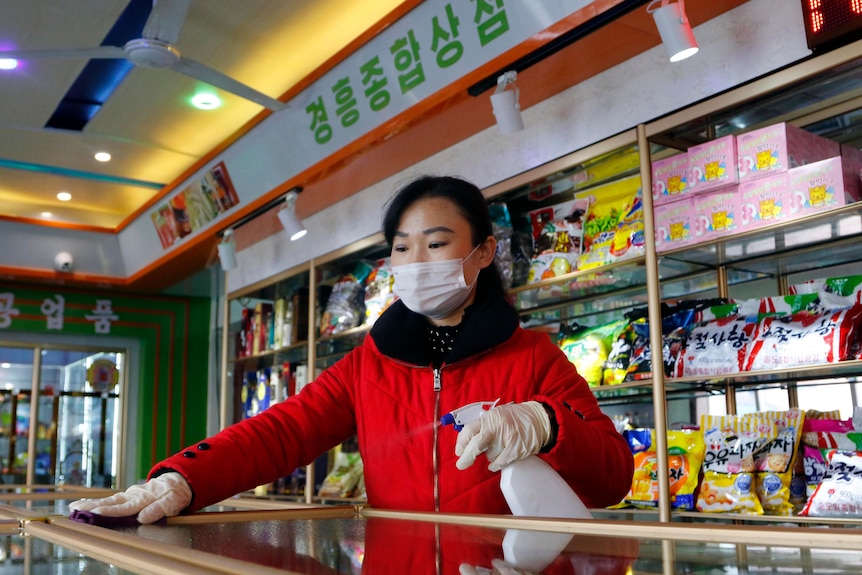 Un trabajador con una máscara facial limpia una encimera en una tienda de comestibles
