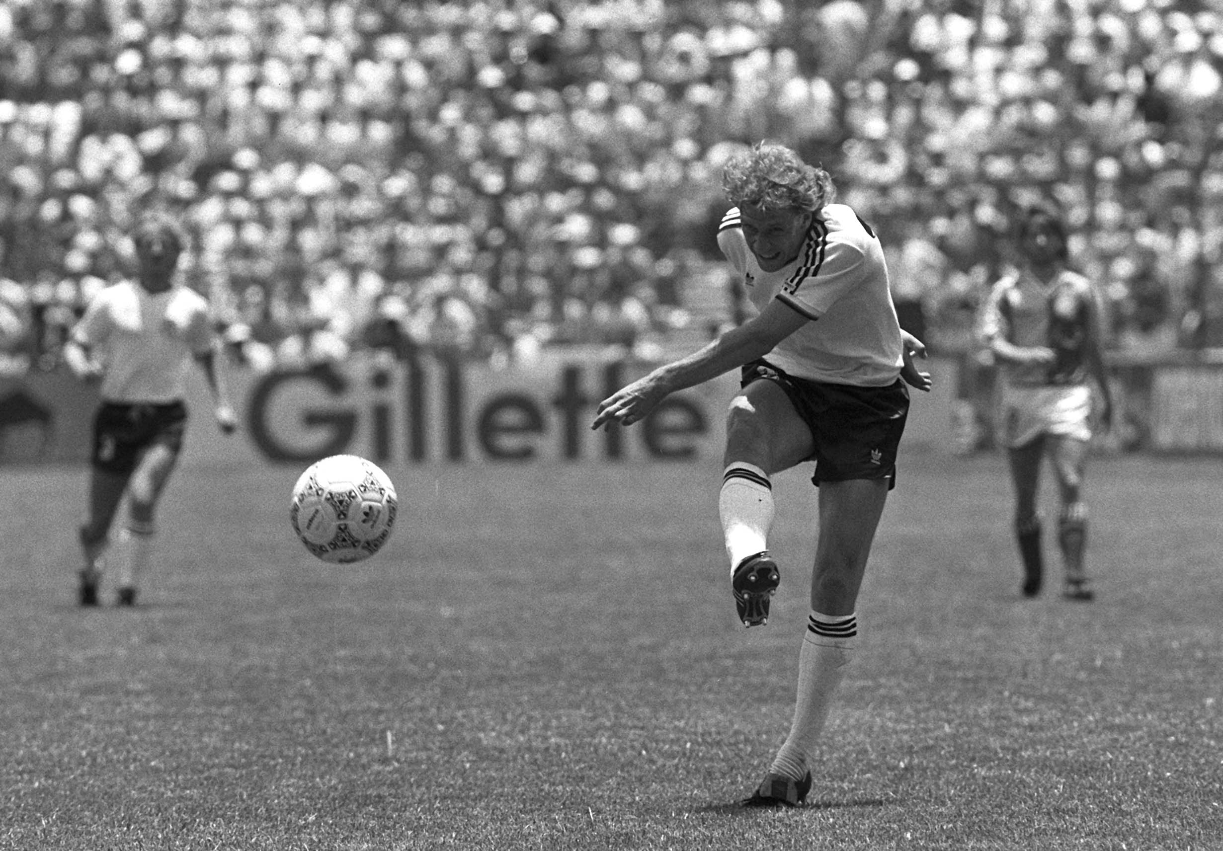 A black and white photo of a footballer completing his follow-through after blasting the ball towards goal.