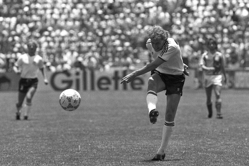 A black and white photo of a footballer completing his follow-through after blasting the ball towards goal.