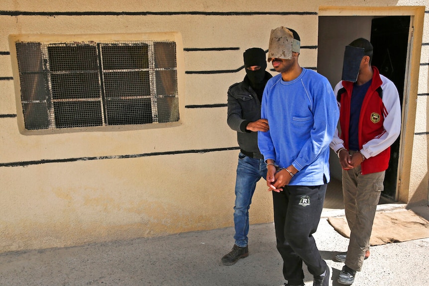 A security officer escorts Alexanda Kotey (left) and El Shafee Elsheikh (right) who have shields on their eyes.